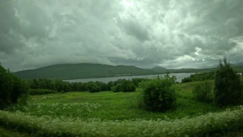 View past green meadows and white wildflowers overlooking lake in Senja Norway Vidéo 342340372