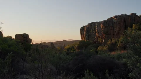 View past a large rock formation at a rocky, hilly landscape at sunrise. UHD50p Stock Footage 250098130