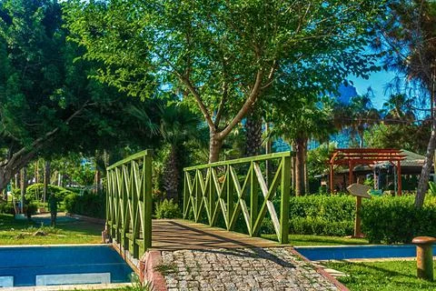 View of the path and the bridge in a green garden with green trees along the Stock Photos