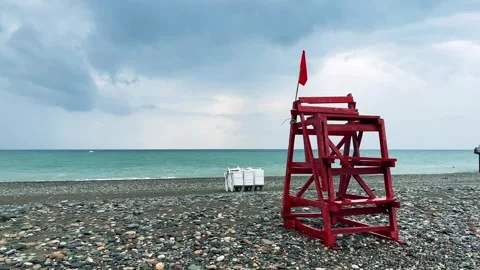 View of pebble beach of Batumi. Rescue wooden tower with red flag sways in wind Stock Footage 263447760