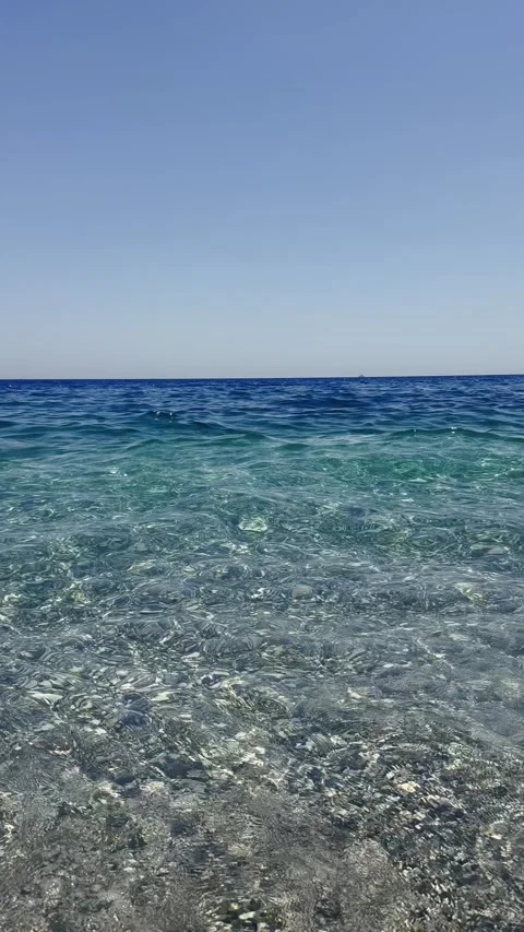 A view from a pebble beach onto the clear azure sea tiny waves crashing against Stock Footage 332762806