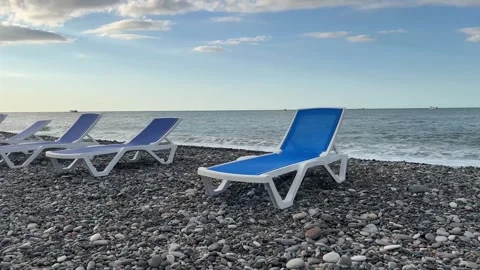 View of pebble beach, sea and blue and white sun loungers on shore line Stock Footage 263447693