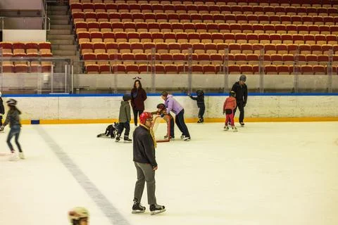 View of people ice skating inside indoor rink with empty spectator seats. Stock Photos
