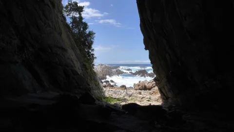 View of a person walking along a rugged, rocky coastline from inside a dark Stock Footage 333027823
