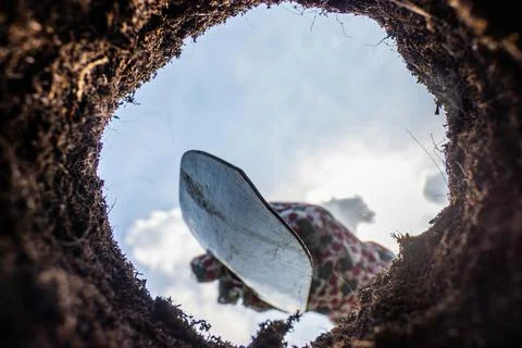 View from a pit in the ground on a raking clay with a small gardening shovel Stock Photos