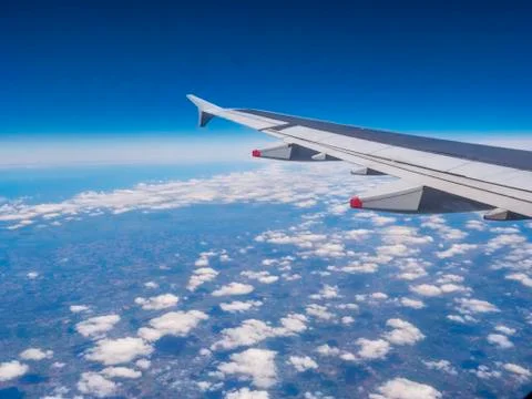 View from a plane window: a plane wing over clouds and blue sky Stock Photos