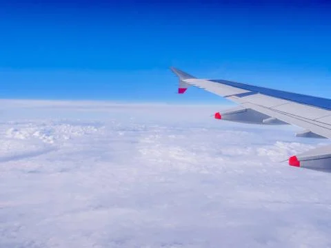 View from a plane window: a plane wing over clouds and blue sky Stock Photos