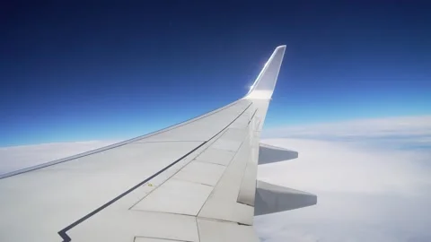 View From Plane Window Showcasing Fluffy White Clouds in Clear Blue Sky During Stock Footage 303373265