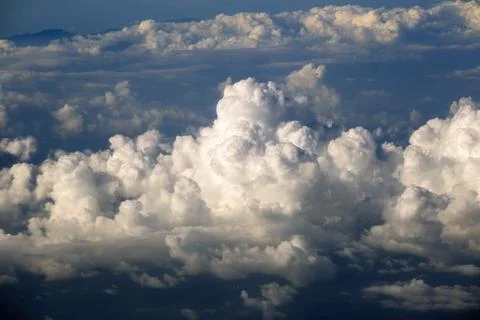 View from plane window of white rain clouds forming on blue sky. Air travel.. 스톡 사진