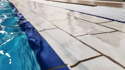 View of pool edge with blue water surface and white tiled deck area, ripples Stock Footage 342230044