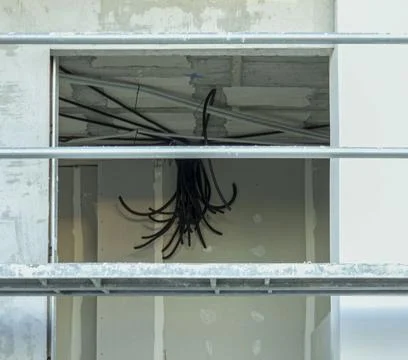 View of power cables hanging from ceiling in room under construction framed.. Stock Photos