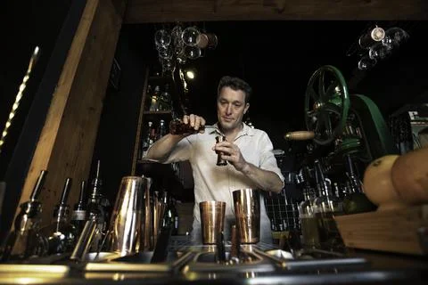 View of a professional bartender preparing a cocktail behind the counter of a Stock Photos