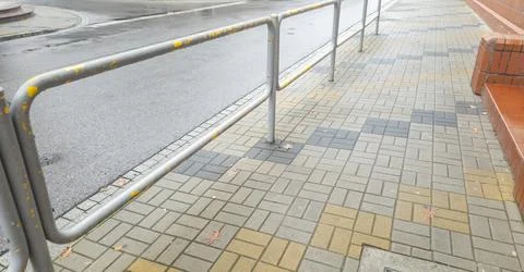 A view of a public sidewalk featuring a metallic railing alongside a pattern of Stock Photos