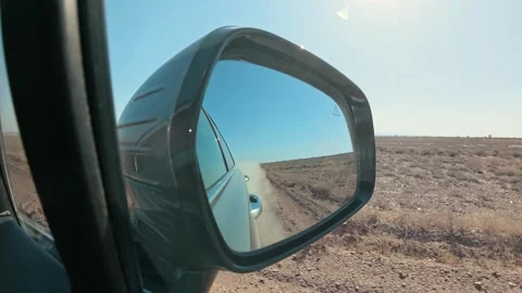 View in rear view mirror from a car driving through a deserted arid terrain Stock Footage 309324362