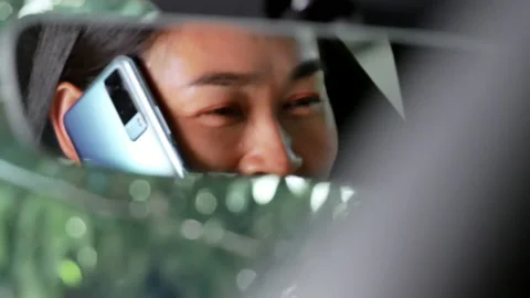 View from rear view mirror of happy woman talking on mobile phone while driving. Stock Footage 161314318
