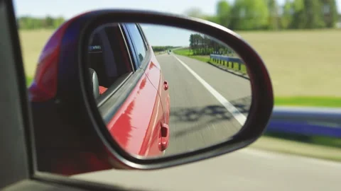 View in the rear view side mirror of a auto, driving a red car along the track Stock Footage 154379876