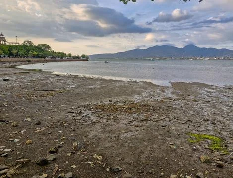 View of receding beach with cloudy sky and mountains in the background Stock Photos
