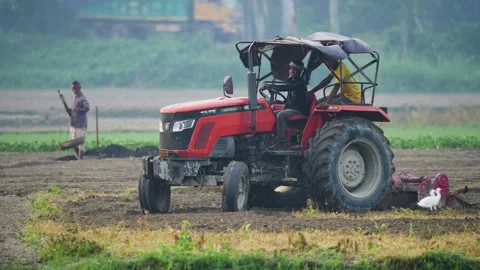 View of a red tractor plowing a field with workers, Bangladesh. Video stock 334981616