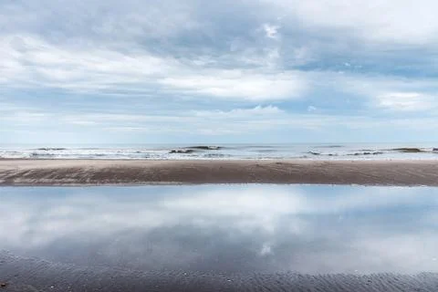 View of the reflection of the clouds with the beach and ocean waves behind on a Stock Photos