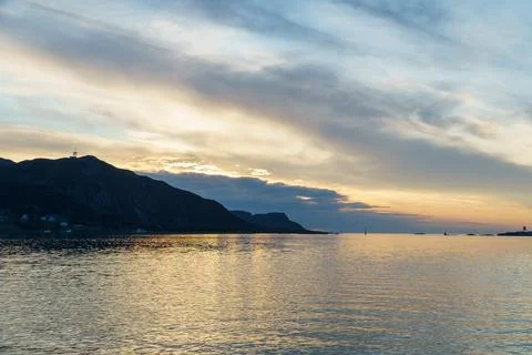 View of rising sun in clouds over mountains and calm sea. Natural look 库存照片