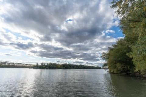 View of a river with clouds, trees, and distant land during afternoon in natu Stock Photos