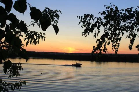 View of the river in the last rays of the sunset with a passing boat Stock Photos