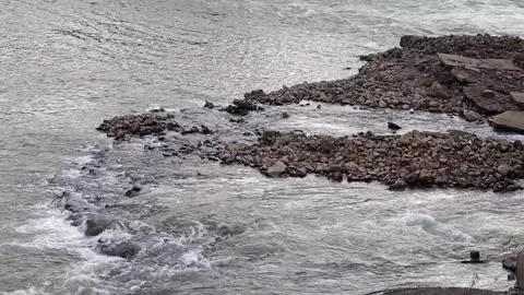 A view of river water splitting and rushing past a small rocky island and broken Stock Footage 342477280