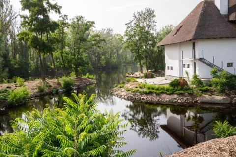 View of the river which reflects a white house with a reed roof and trees Stock Photos