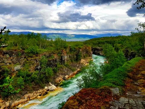 View of a river winding through rocky terrain with trees under a cloudy sky.. Stock Photos