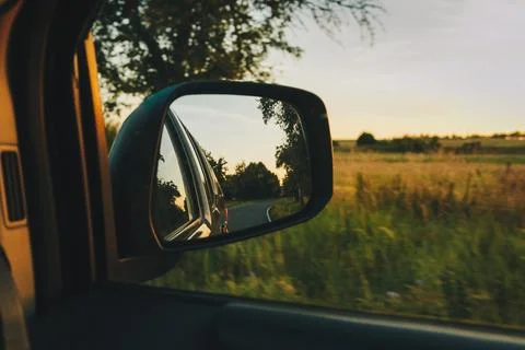 View on the road in the side mirror in front of the meadow at sunset. Stock Photos
