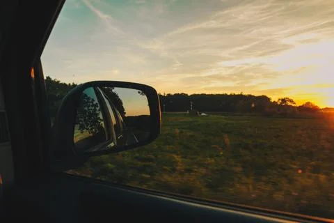 View on the road in the side mirror in front of the meadow at sunset. Stock Photos