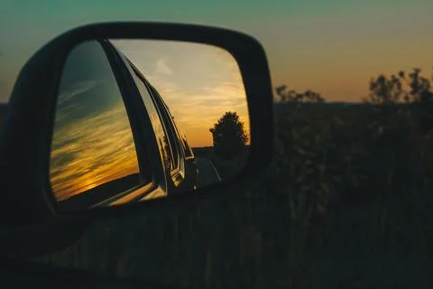 View on the road in the side mirror in front of the meadow at sunset. Stock Photos