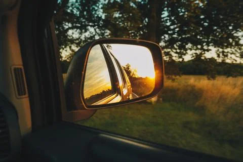 View on the road in the side mirror in front of the meadow at sunset. Stock Photos