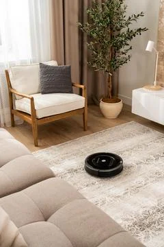 View of a robot vacuum cleaner working on a carpet in a new living room in light Stock Photos