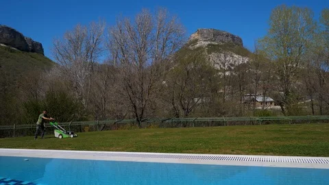 View of the rock. Grass cutter. Man mows grass with a lawn mower near the pool 스톡 동영상 129503737
