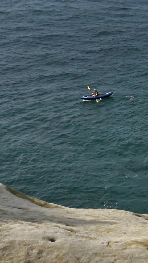  View from the rock of woman rows an outrigger canoe on still ocean water Stock Footage 319036799
