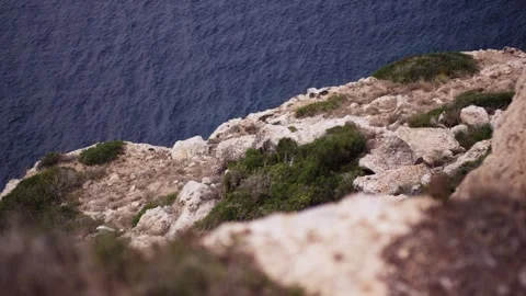 View from a rocky cliff edge down to the deep blue sea, rugged coastal landscape Stock Footage 341578718