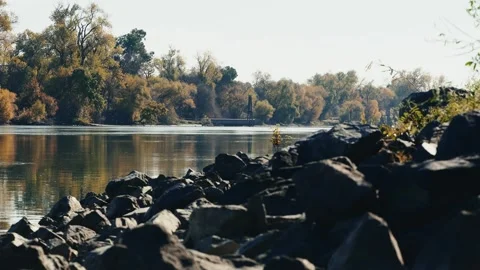 View of rocky levee with drainage pipe on opposite side of a river Stock Footage 258298393
