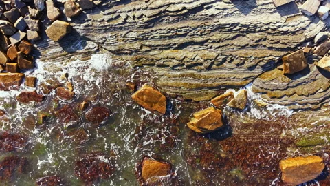 View of rocky shore with ocean waves and textured stone layers at low tide in Stock Footage 341110973