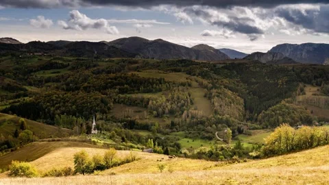 View of rolling green hills and a small white church in Romania. Video stock 333527230