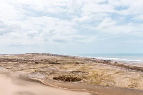 View of the sand and dunes in front of the sea with some clouds in the sky. Stock Photos