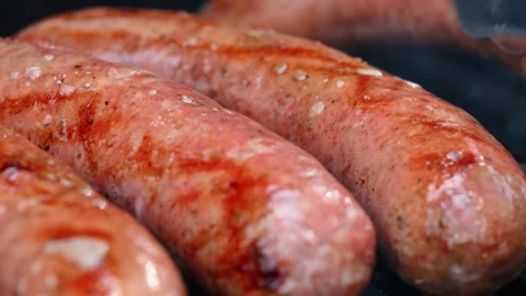 View of Sausages turning over while grilling on barbecue with open flame. Close Stock Footage 334022218