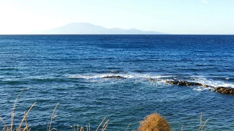 View on the sea waves hitting the rocks on the beach from the tall grass Stock Footage 128927367