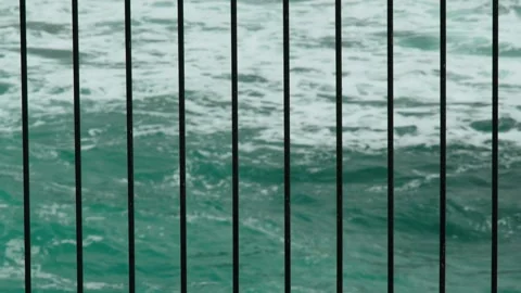 View of the sea waves through the lattice of the balcony. White sea foam bubbles Stock Footage 178396425