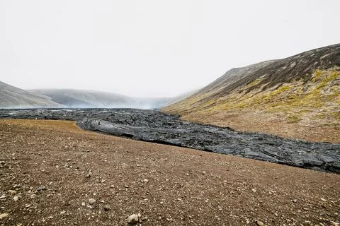 View of seemingly visible river of cooled lava turned into black volcanic rock - Stock Photos