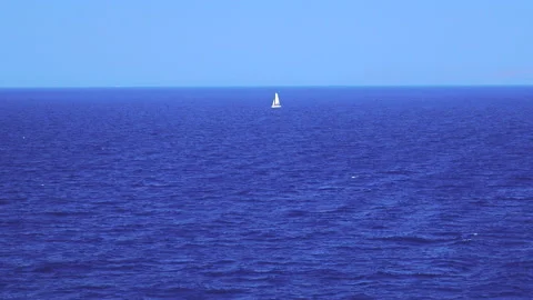 View from a ship of a small white boat with white sails in the blue of the wa Vídeos de archivo 138234704