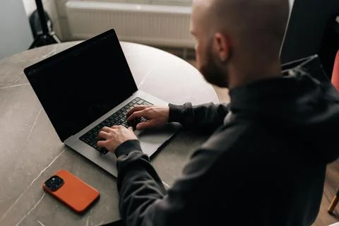 View from shoulder of focused bald programmer with beard and hoodie sitting at 写真素材