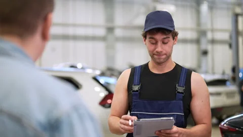 View from shoulder of man client to mechanic male explaining checklist car Stock Footage 281029309