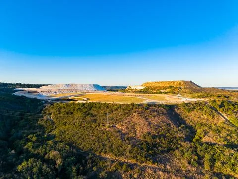 A view shows a large quarry site with mounds of earth and a mix of vegetation Stock Photos