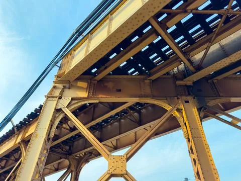 The view shows the underside of a metal bridge that holds train tracks above. Stock Photos